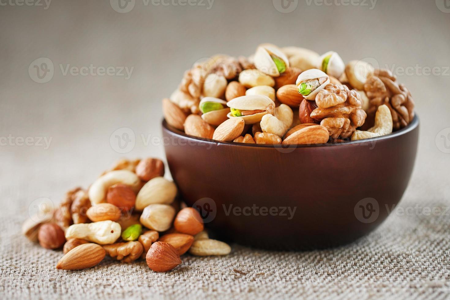 nueces de diversas variedades se derraman de un plato de madera sobre una mesa con un paño de arpillera. foto