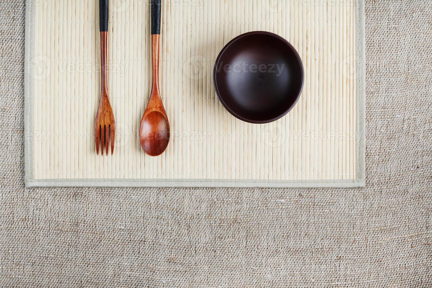 Empty dark wooden cup, spoon and fork made of natural wood on a light bamboo backing photo