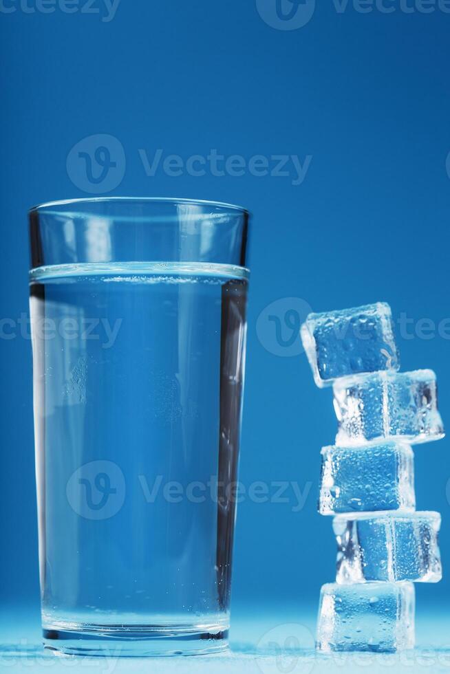 A glass of ice and clear water, ice cubes on a blue background