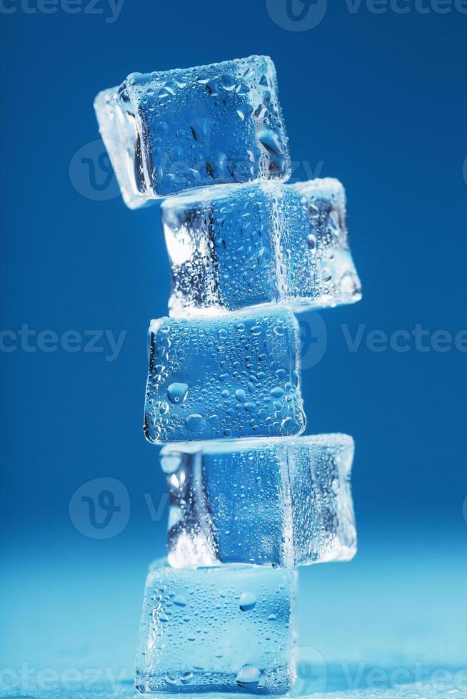 Ice cubes with water drops tower in a row on a blue background. photo