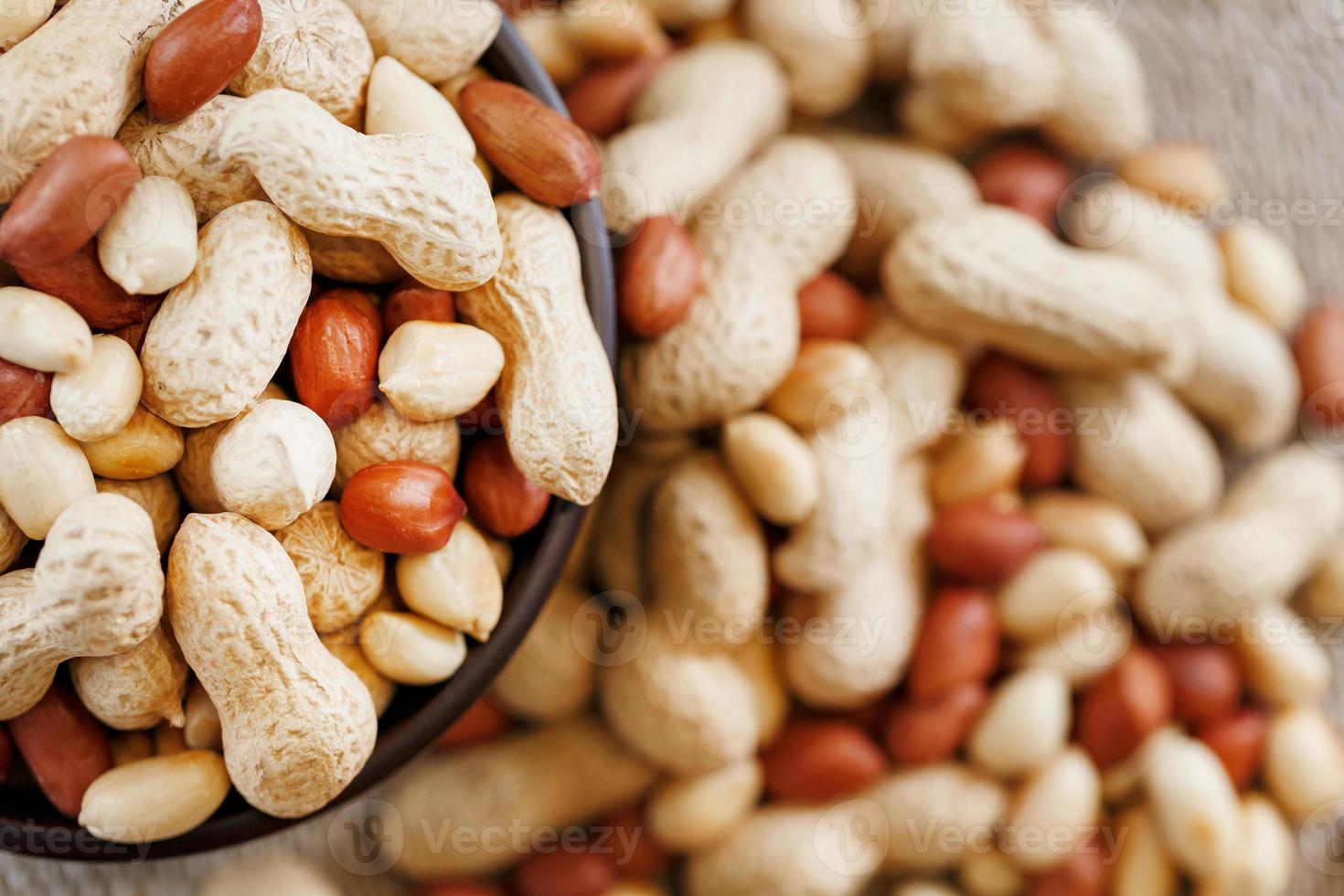 Peanuts in the shell and peeled close-up in cups. Roasted peanuts in their shells and peeled against a brown cloth. photo