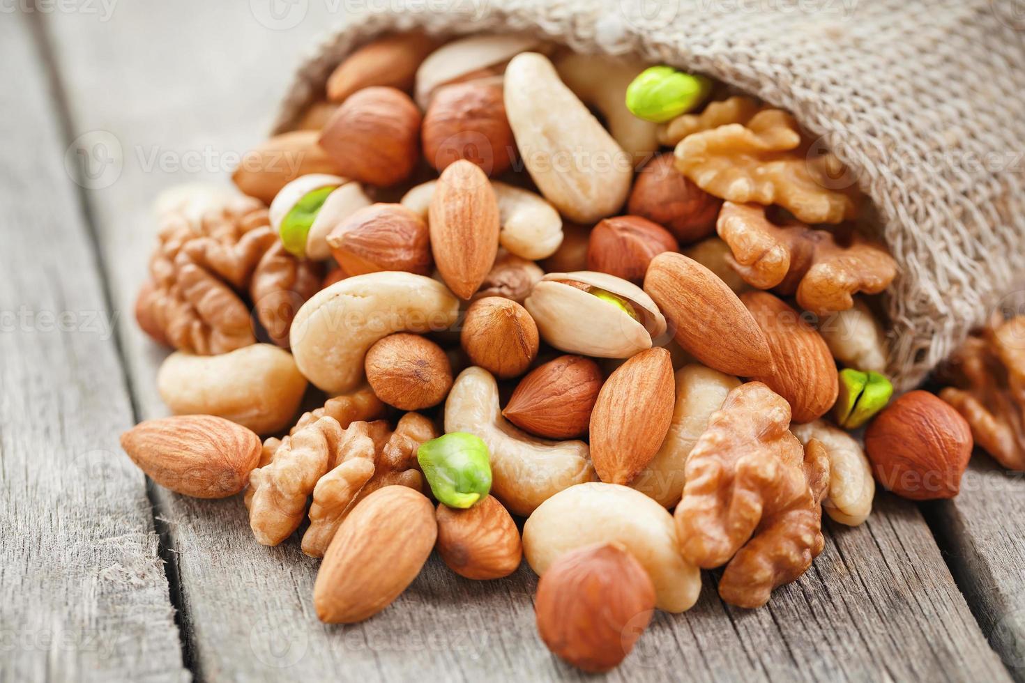 A mixture of fresh nuts spilled from a linen bag onto a gray wooden table. photo