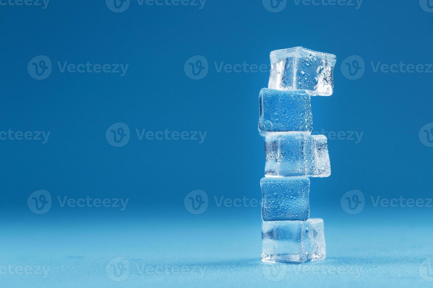 Ice cubes with water drops tower in a row on a blue background. photo