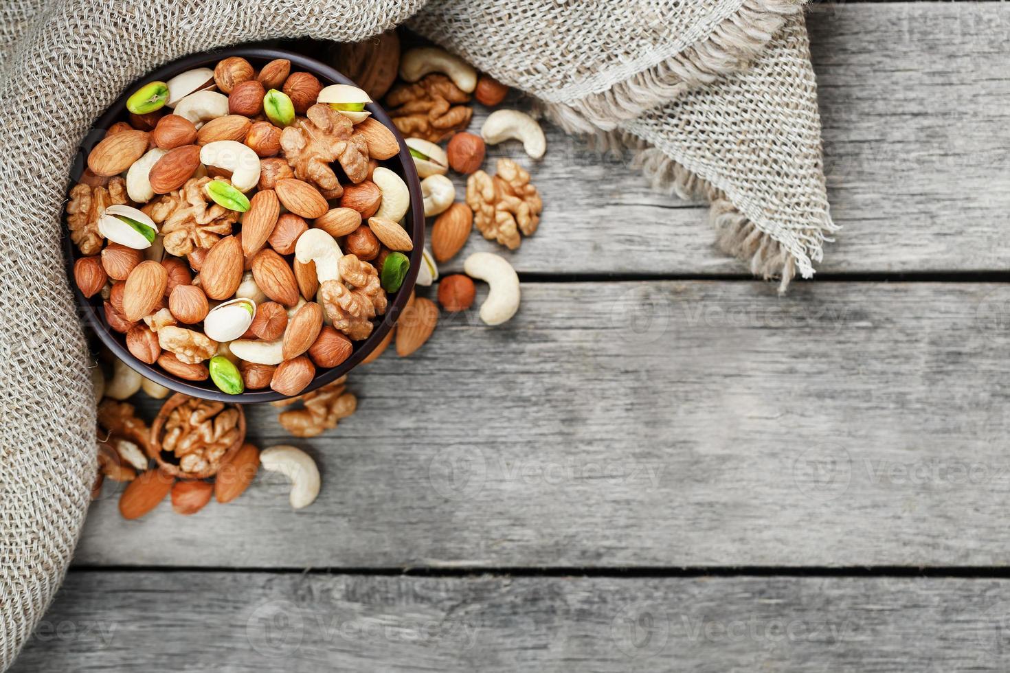 Nuts of various varieties spill out from a wooden plate on a table with a burlap cloth. photo