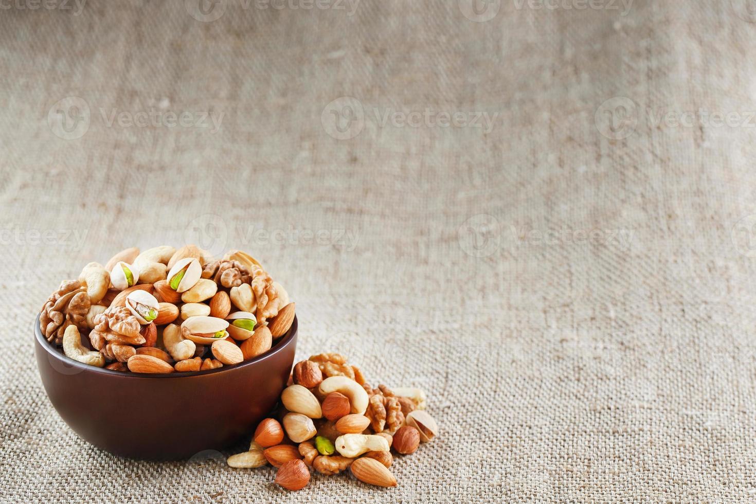 nueces variadas en un plato sobre una mesa de madera con un paño de arpillera. foto