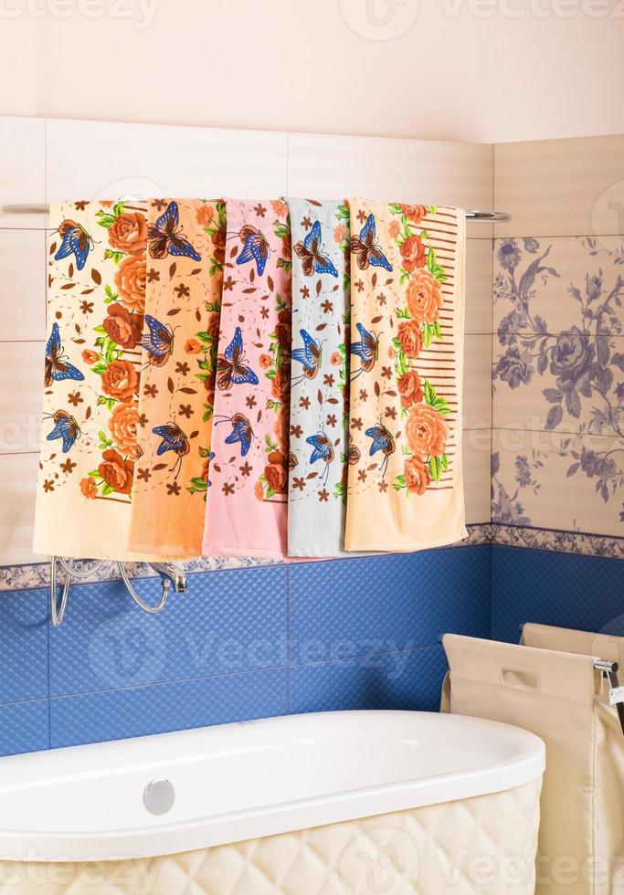 A vertical shot of a row of colorful patterned towels hanging on a shower rack above a bathtub photo