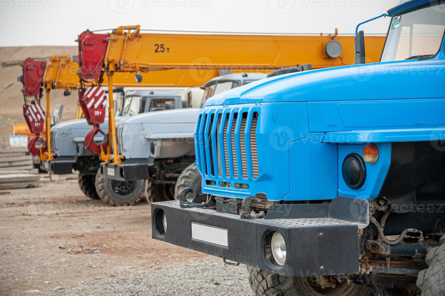 A closeup row of large truck cranes and machines at an industrial construction site photo