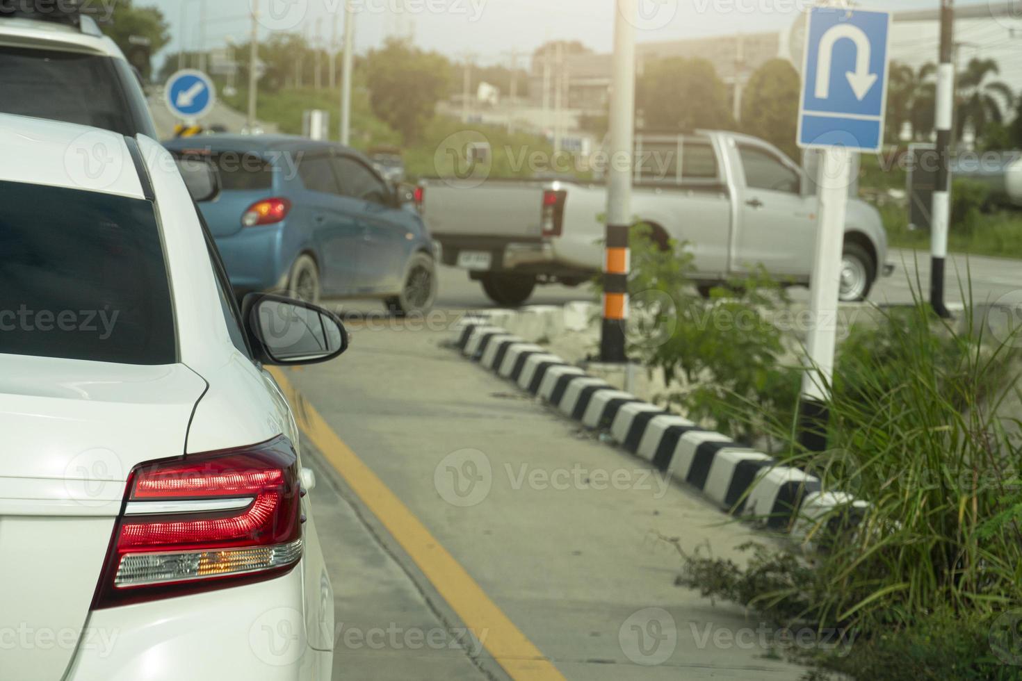 Rear side of white car stop on the road and turn on right signal light for U-Turn. Queuing from multiple cars entering the expressway. With green grass beside of the road. photo