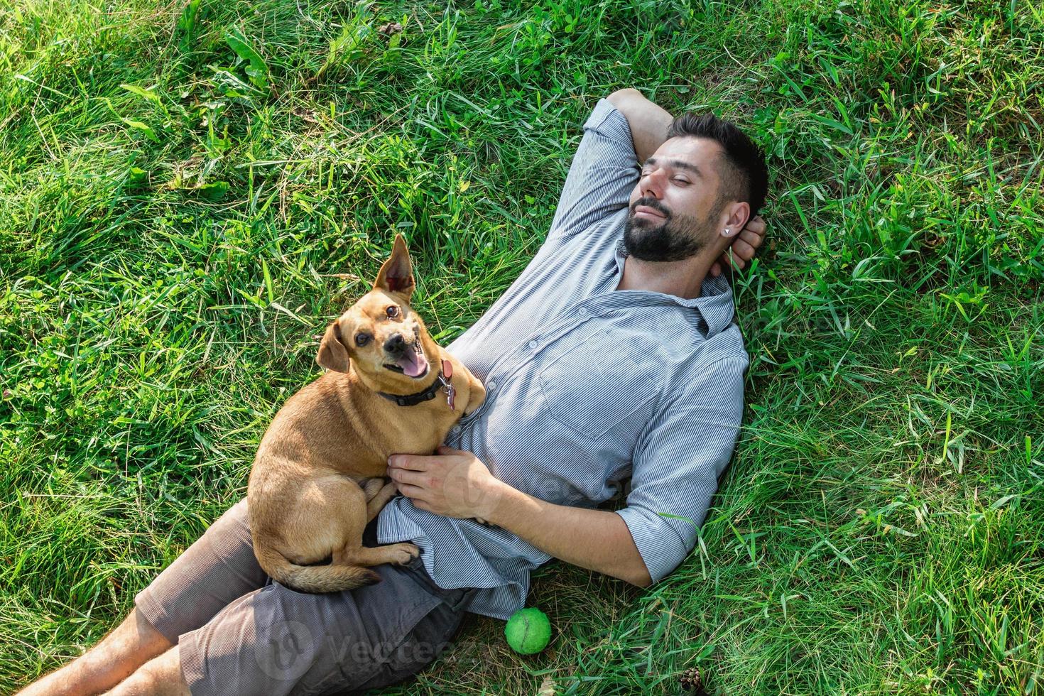 Attractive European man is resting on grass with his cute little dog on a summer sunny day. photo