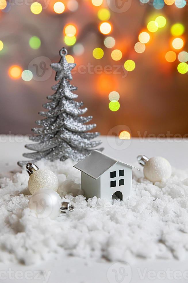 Abstract Advent Christmas Background. Toy model house and winter decorations ornaments on background with snow and defocused garland lights. Christmas with family at home concept. photo