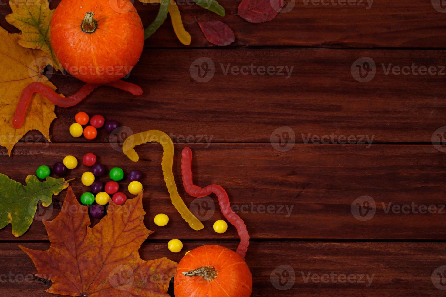 Traditional Halloween sweets. Pumpkins, autumn leaves and candies on wooden background. photo