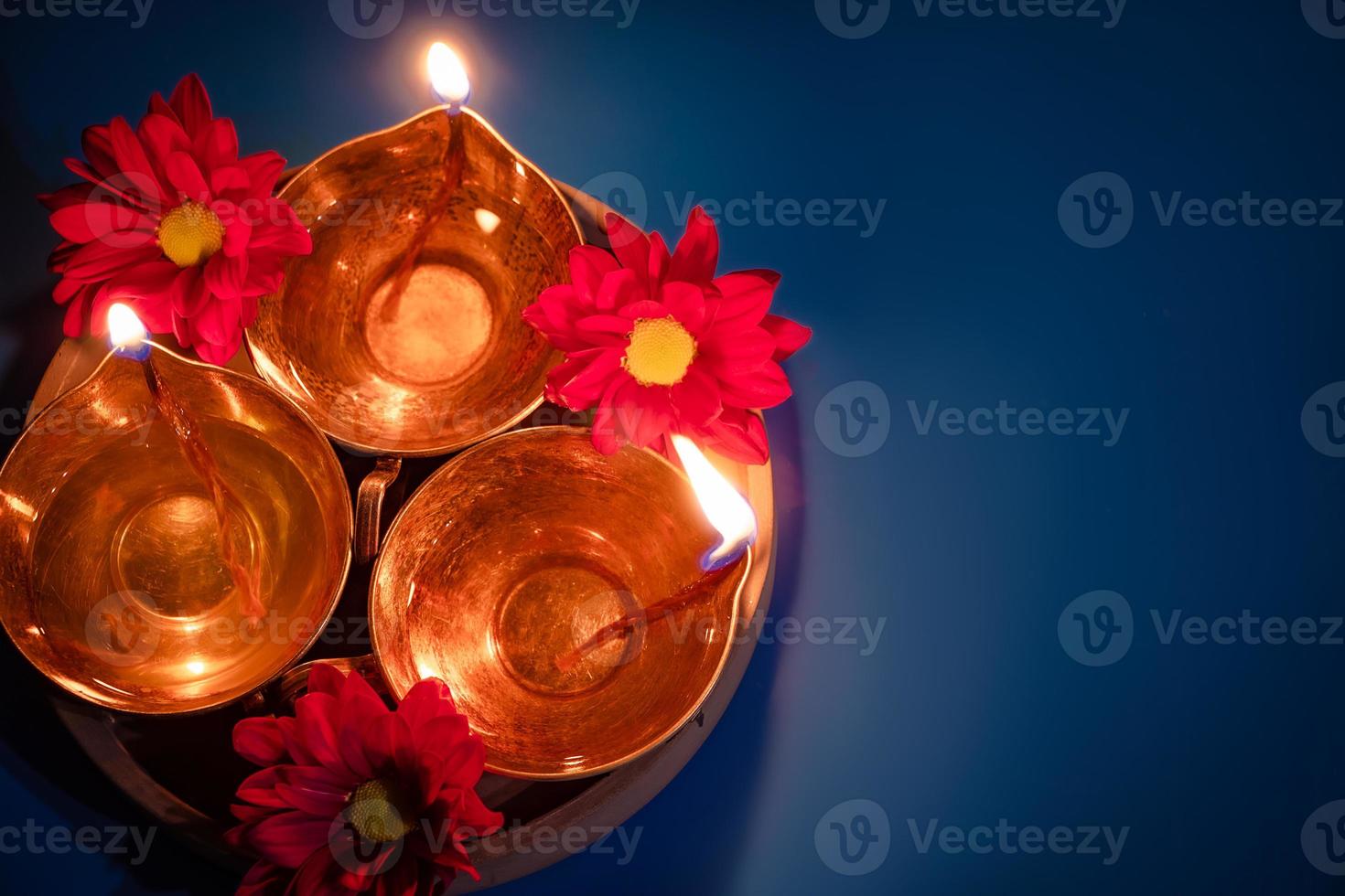 Happy Diwali. Celebrating the Indian Festival of Light. Traditional diya oil lamps and red flowers on blue background photo