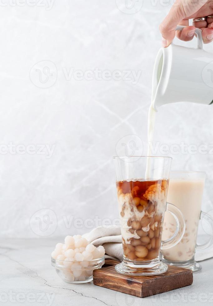 hand pouring milk into glass with iced bubble tea, cement wall background photo