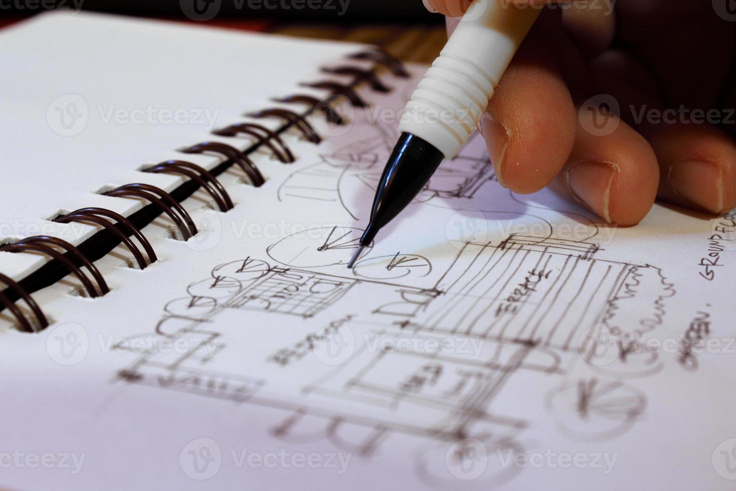 Architect's hands are sketching architectural plans with pencils on a sketchbook on a desk with a laptop. photo