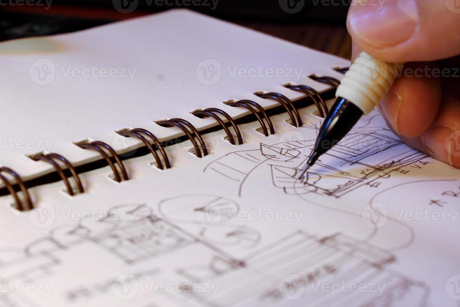 Architect's hands are sketching architectural plans with pencils on a sketchbook on a desk with a laptop. photo