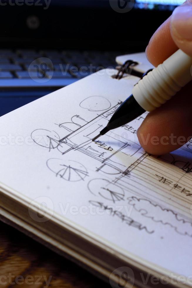 Architect's hands are sketching architectural plans with pencils on a sketchbook on a desk with a laptop. photo