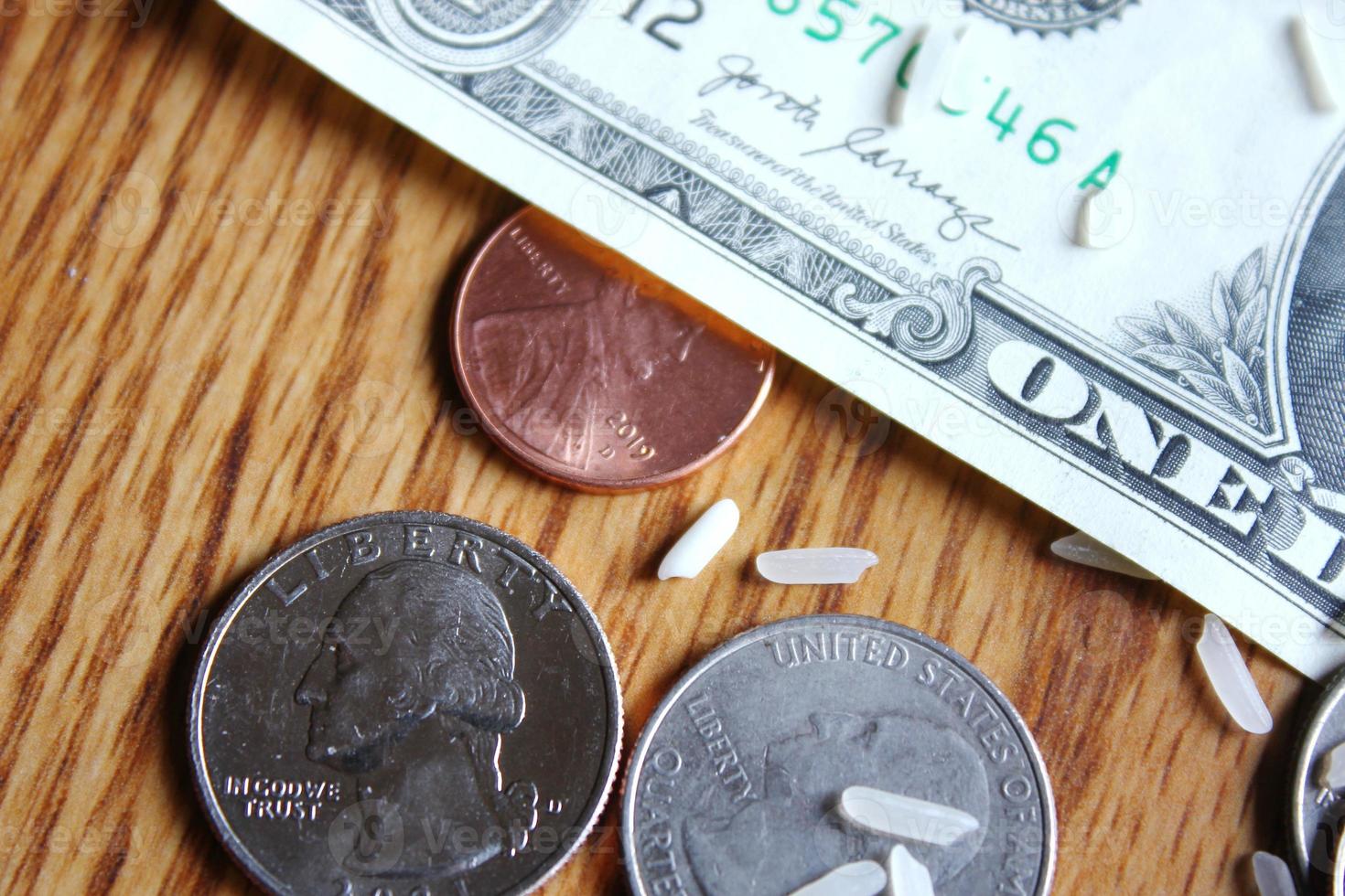 Dollar coins and dollar bills are scattered on a wooden table with grains of rice. photo