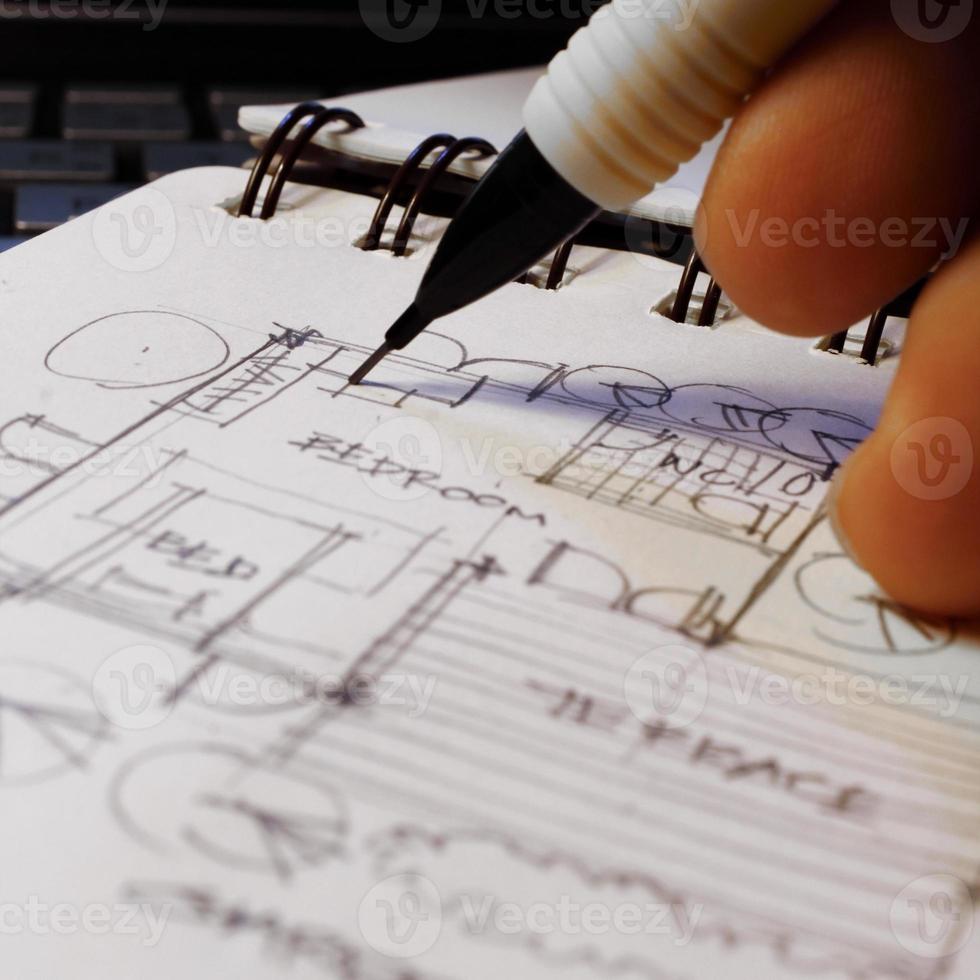 Architect's hands are sketching architectural plans with pencils on a sketchbook on a desk with a laptop. photo