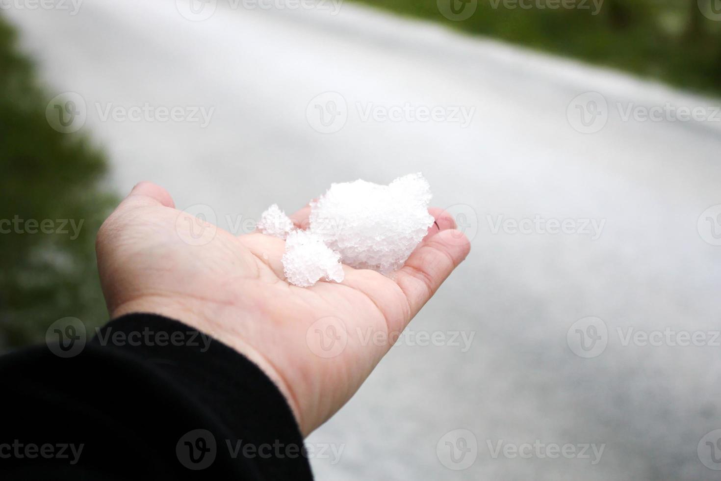 A man's hand holding snow in his hand after it snows against a snow-covered road in the background. photo