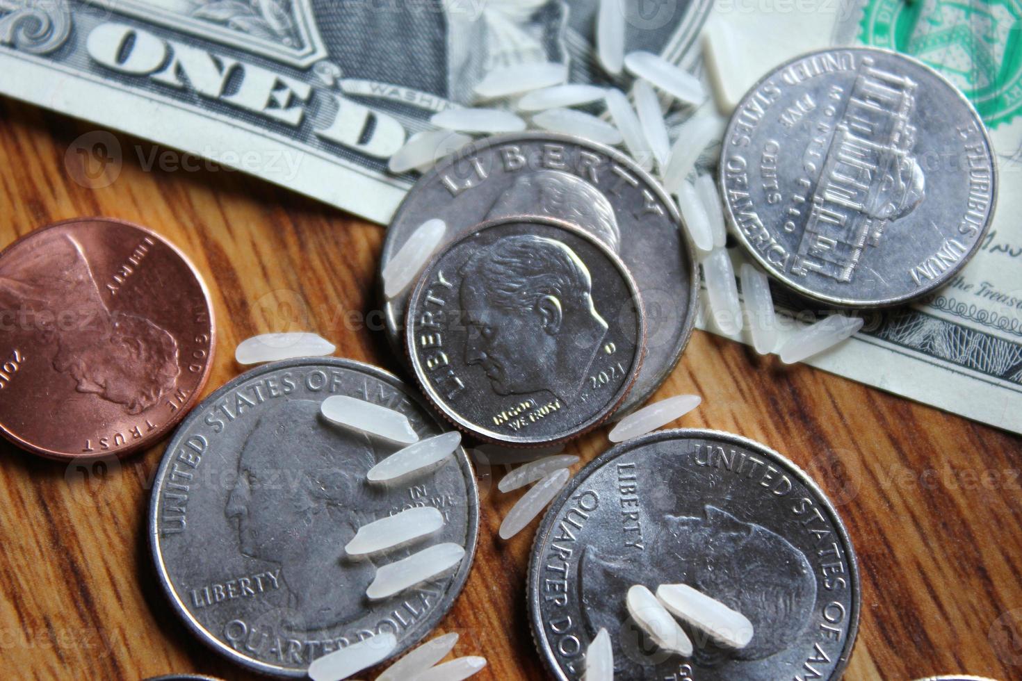 Dollar coins and dollar bills are scattered on a wooden table with grains of rice. photo