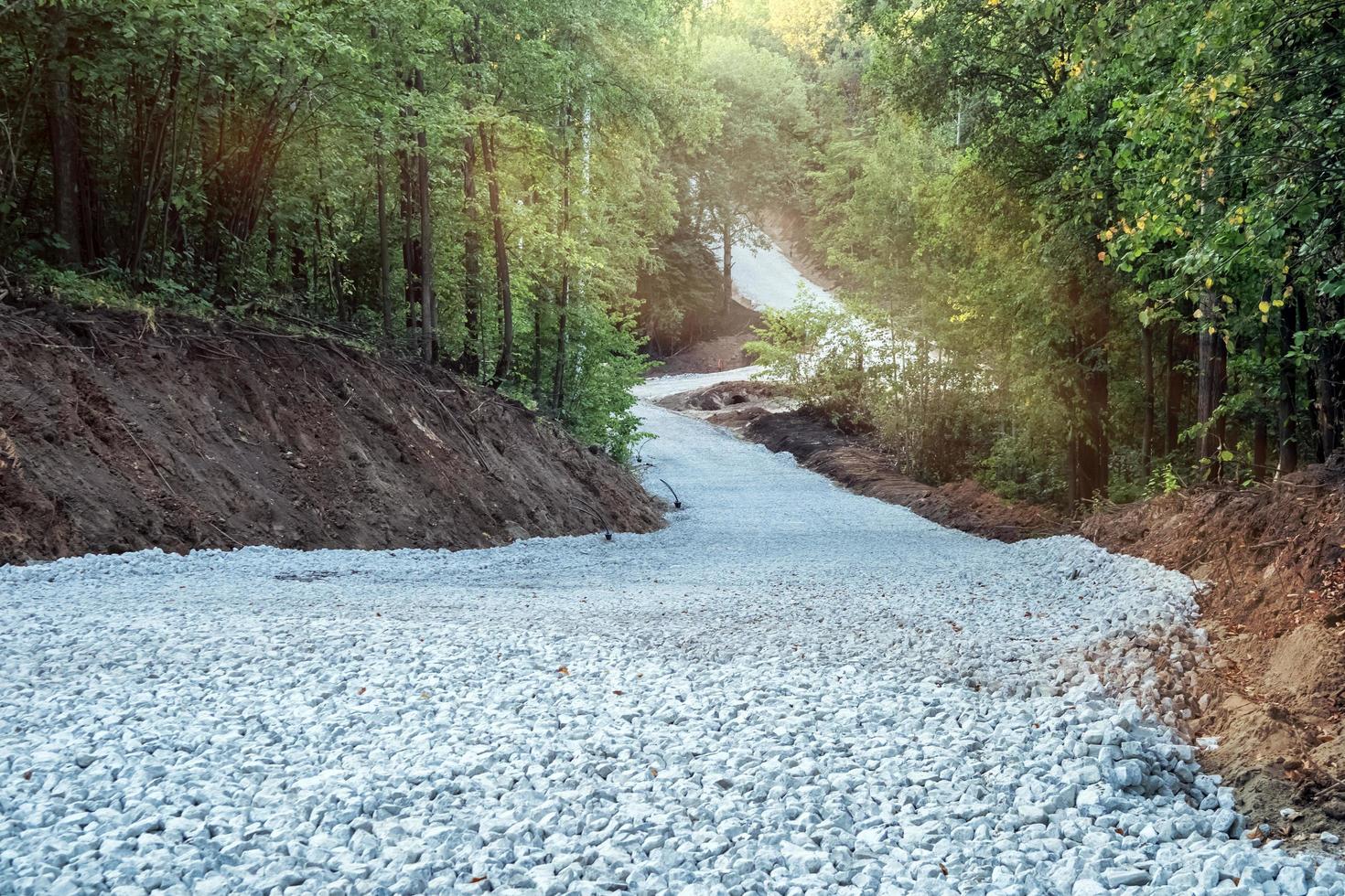 construcción de un nuevo camino sinuoso a través del bosque. Sustrato de piedra triturada preparada para pavimentación asfáltica. foto