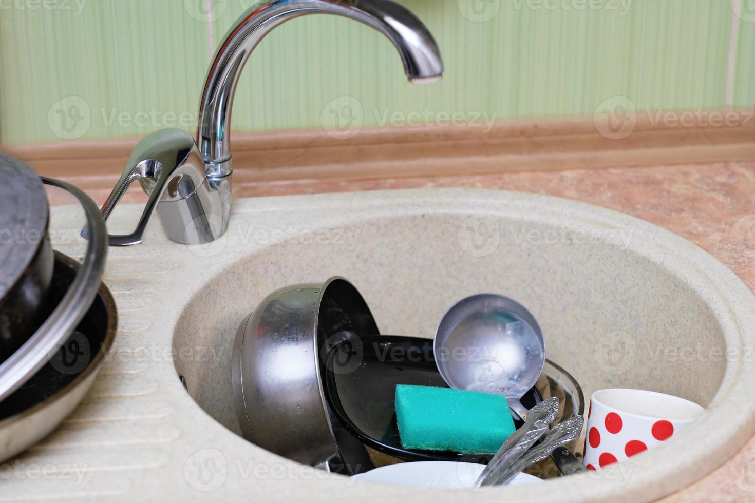 dirty dishes and kitchen utensils in a sink. messy kitchen. cluttered sink. daily routine, chores and housekeeping. photo