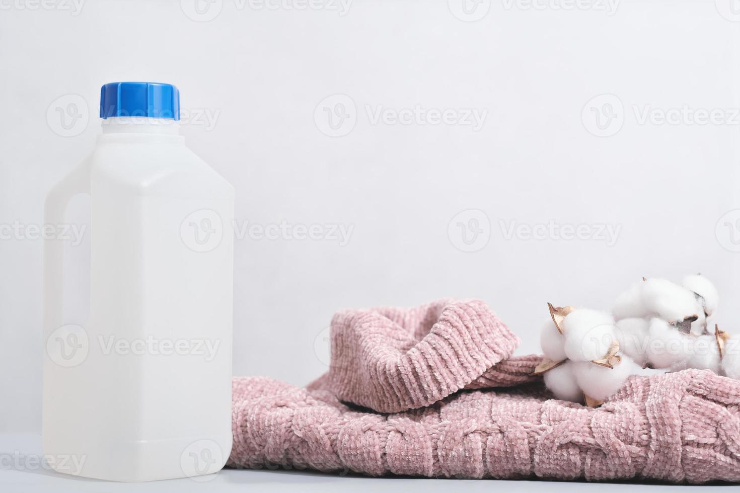 wool detergent in a bottle and pink pullover with cotton buds. special washing solution for soft delicate textile and knitted apparel. photo