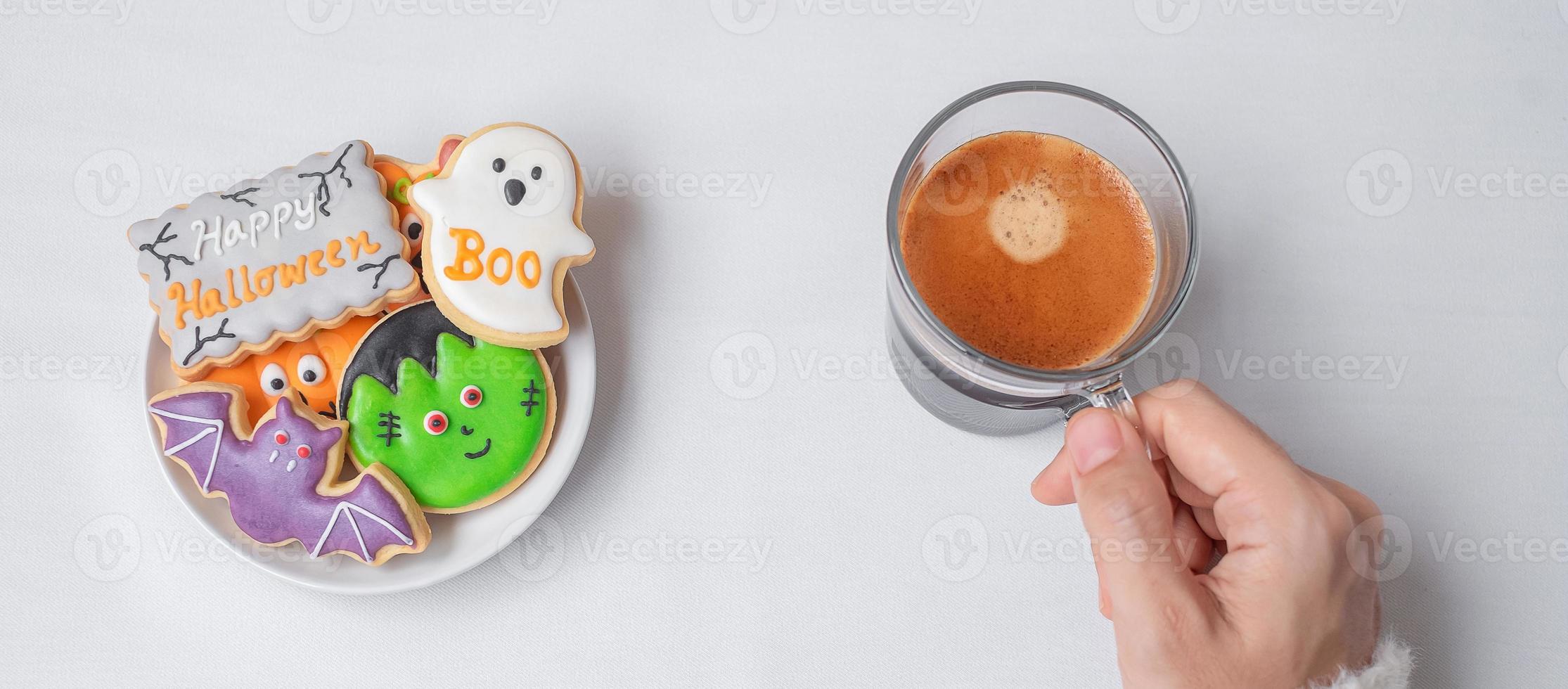 mano de mujer sosteniendo la taza de café durante la comida divertidas galletas de halloween. feliz día de halloween, truco o amenaza, hola octubre, otoño otoño, tradicional, concepto de fiesta y vacaciones foto