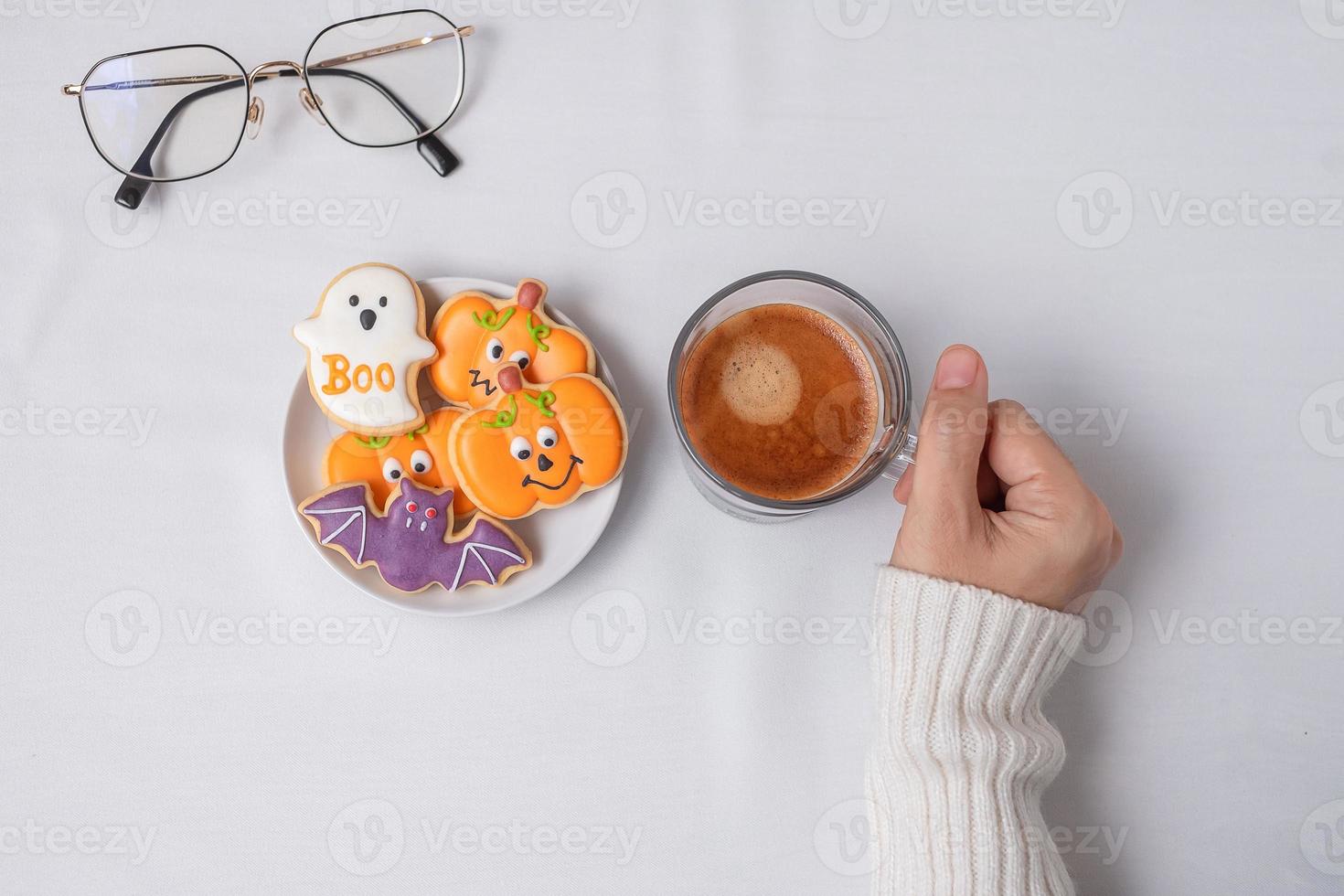 woman hand holding coffee cup during eating funny Halloween Cookies. Happy Halloween day, Trick or Threat, Hello October, fall autumn, Traditional, party and holiday concept photo