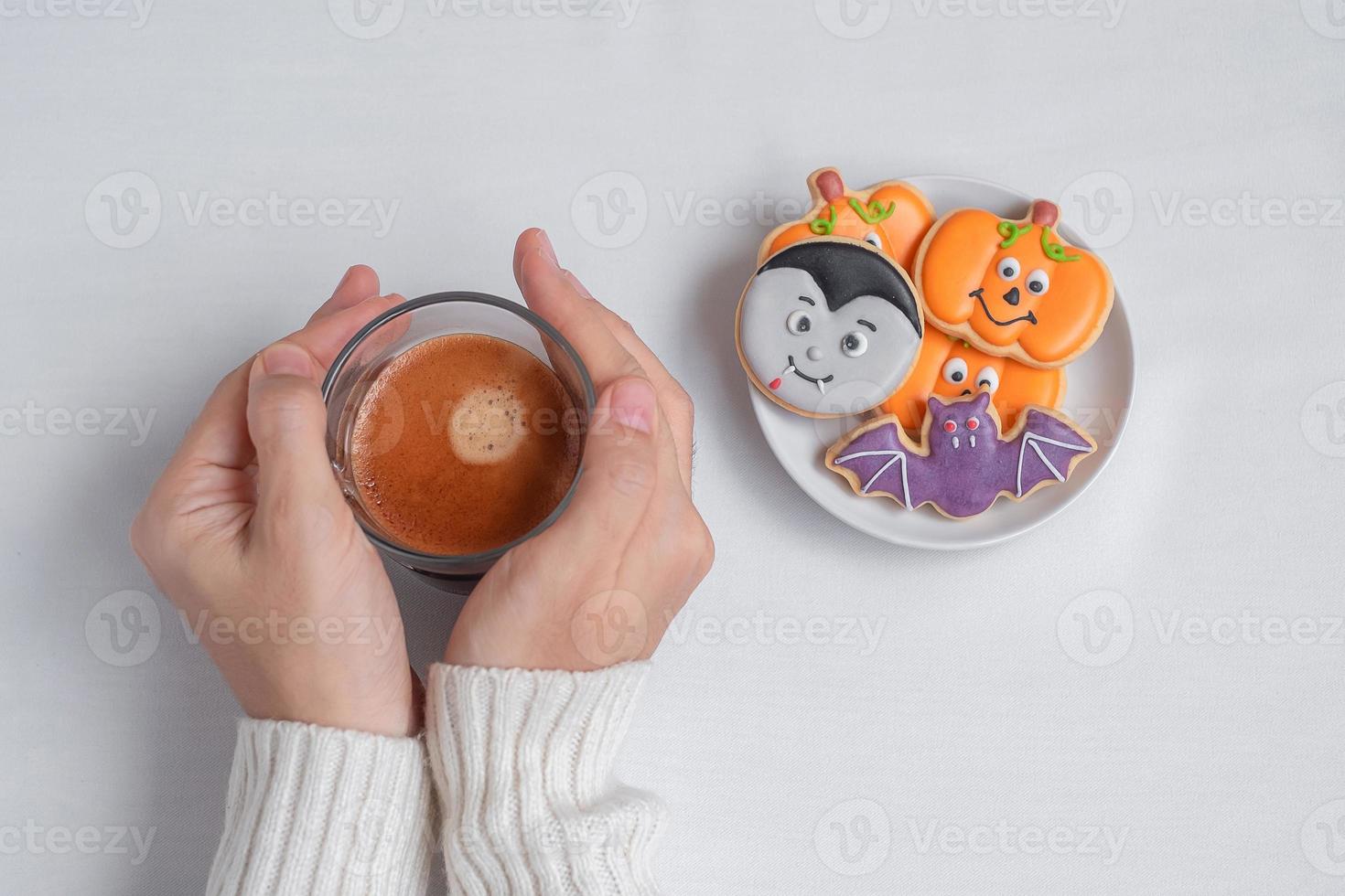 woman hand holding coffee cup during eating funny Halloween Cookies. Happy Halloween day, Trick or Threat, Hello October, fall autumn, Traditional, party and holiday concept photo