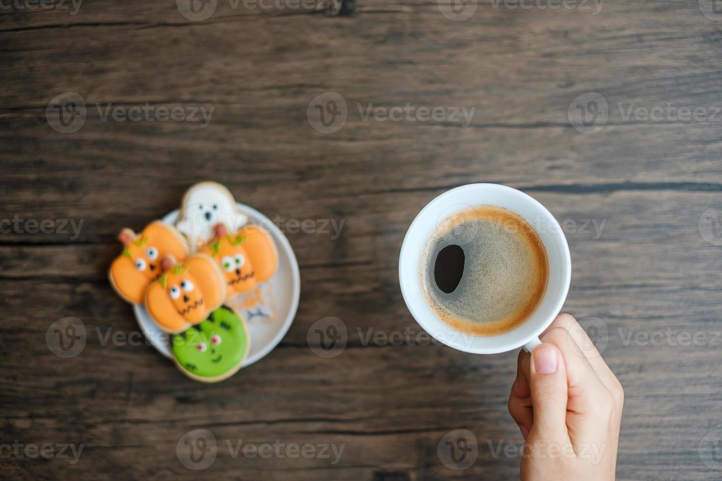 hand holding coffee cup during eating funny Halloween Cookies. Happy Halloween day, Trick or Threat, Hello October, fall autumn, Traditional, party and holiday concept photo