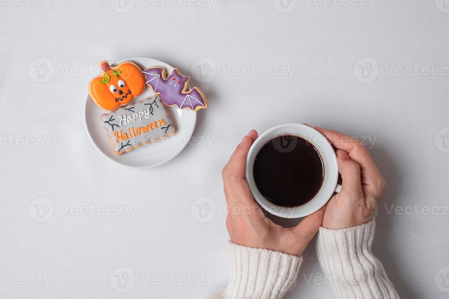 woman hand holding coffee cup during eating funny Halloween Cookies. Happy Halloween day, Trick or Threat, Hello October, fall autumn, Traditional, party and holiday concept photo