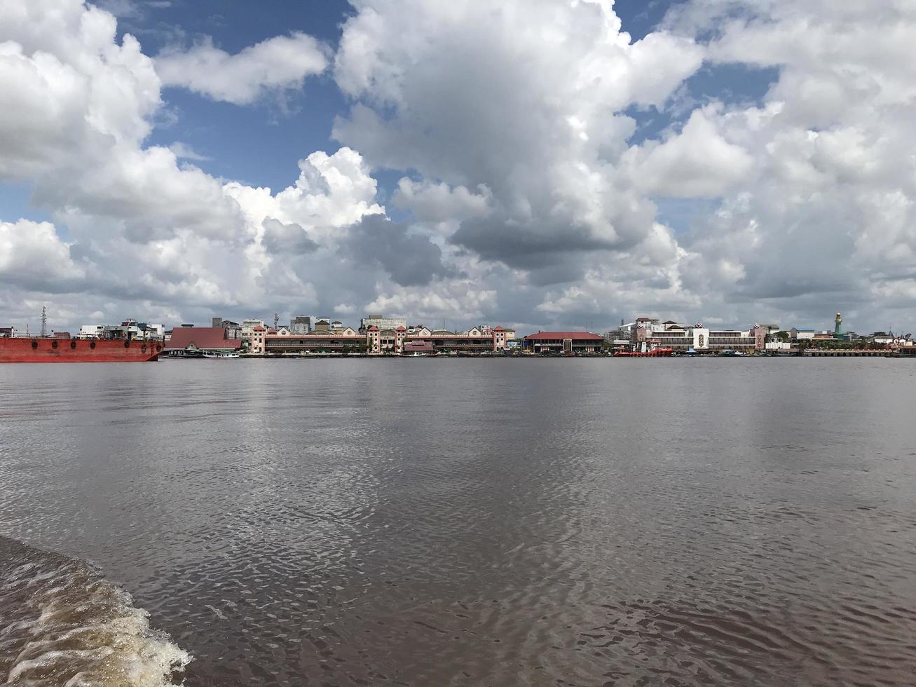 The wide river where the boats pass with views of white clouds and blue skies and in the middle there are traditional market buildings lined up photo