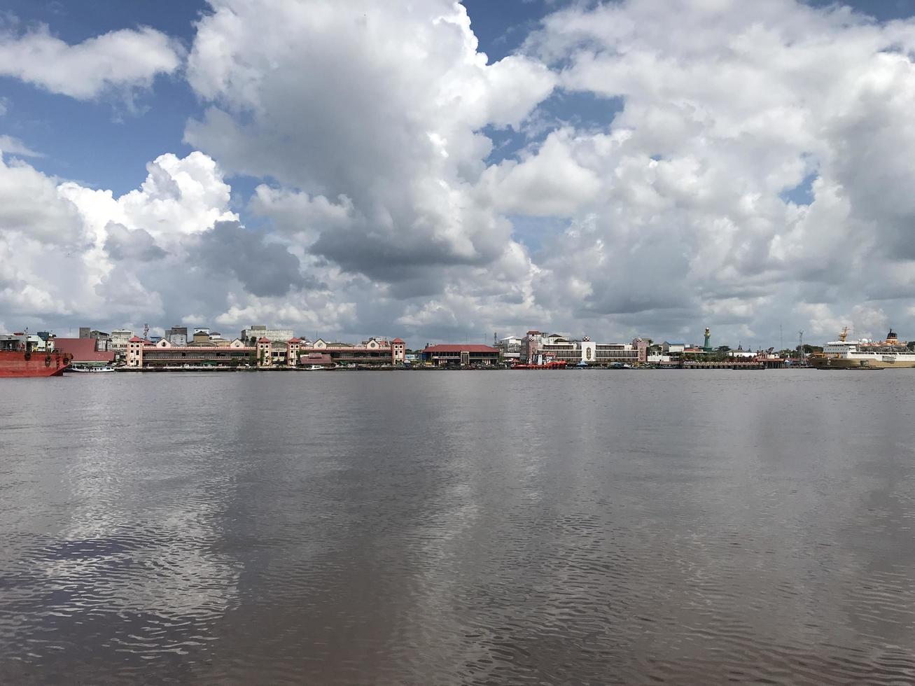 The wide river where the boats pass with views of white clouds and blue skies and in the middle there are traditional market buildings lined up photo