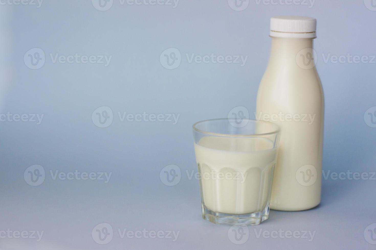 un vaso y una botella de leche blanca, resaltados en un fondo azul, primer plano. foto