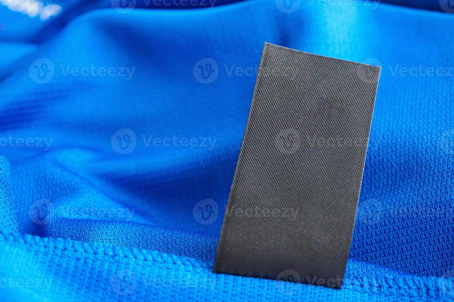 Black blank laundry care clothes label on blue jersey polyester sport shirt background photo