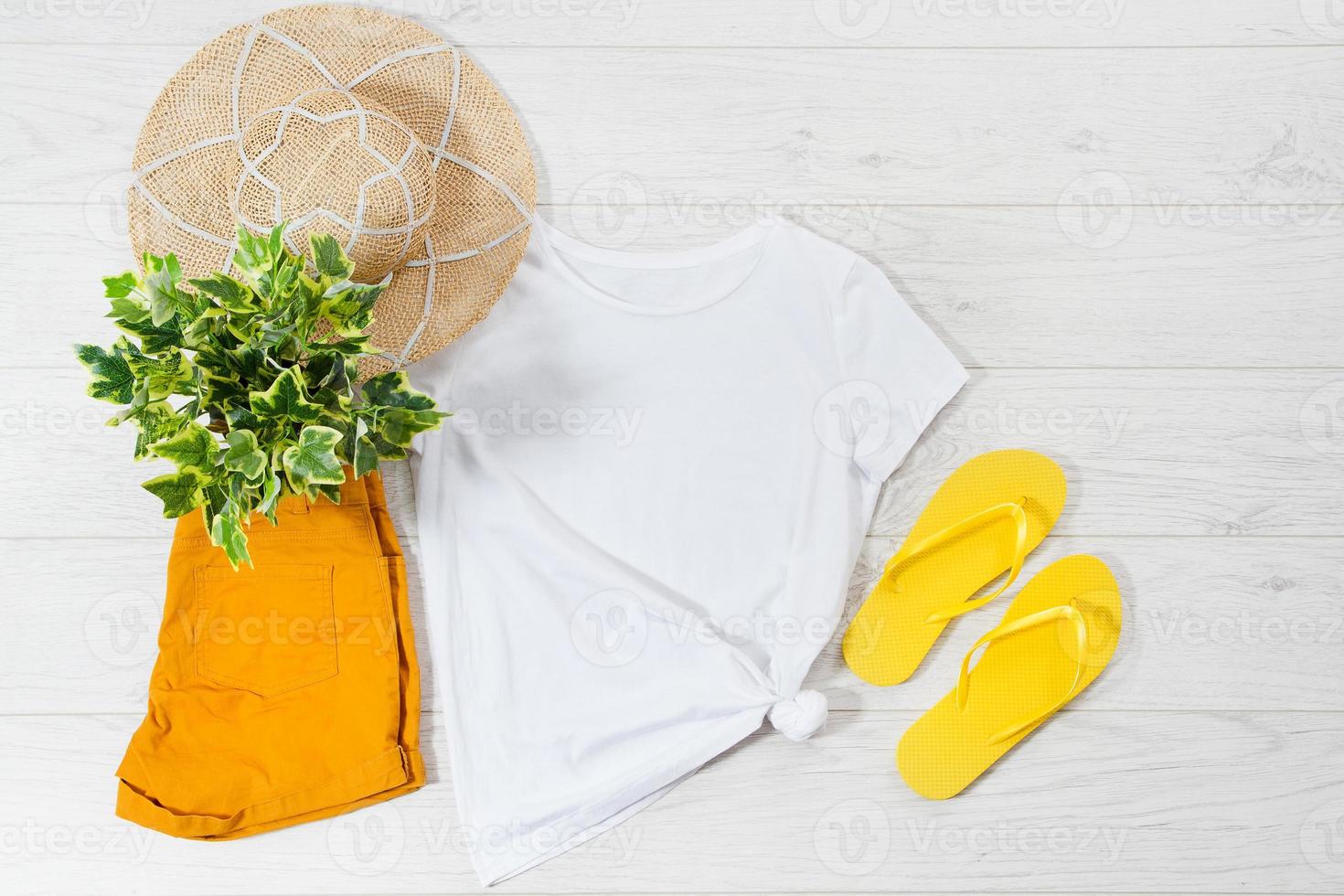 White closeup t shirt mock up flat lay and flip flops on white wooden background. Top view and copy space. Mockup summer t-shirt and summertime. Template blank shirt. photo