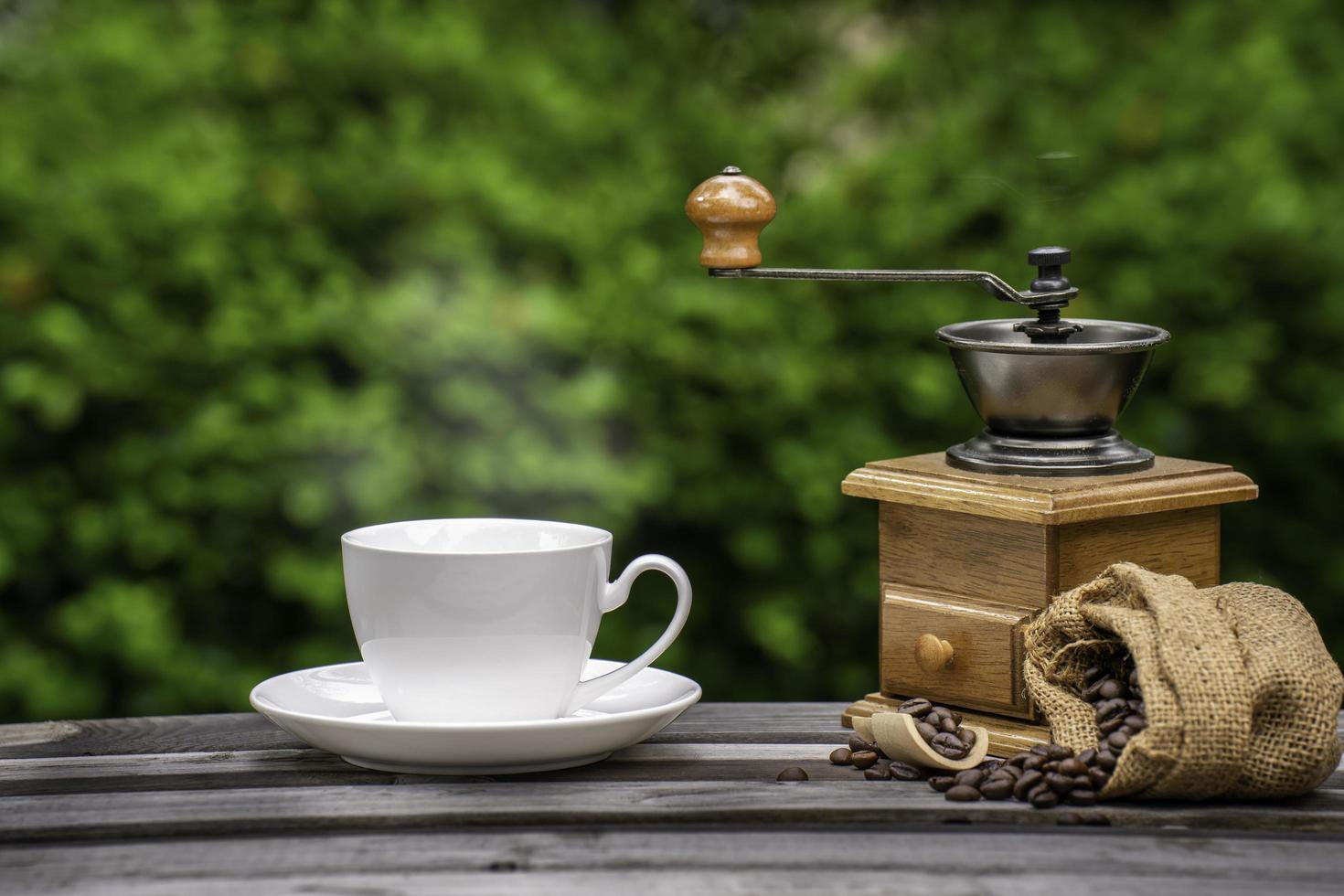 taza de café con molinillo, granos de café oscuros en el viejo piso de madera, cerca de semillas de café en un fondo natural. foto