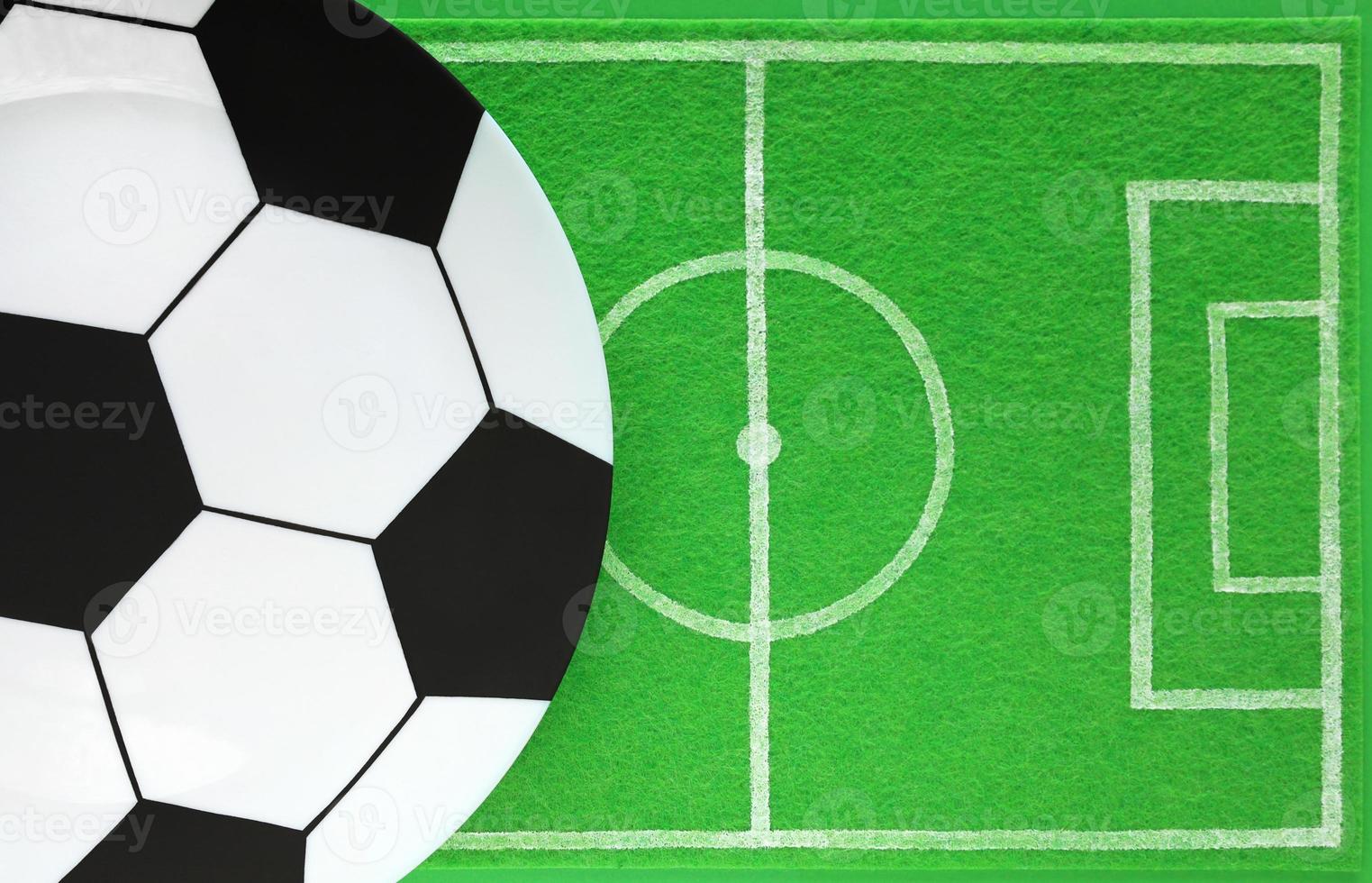 Template of football soccer party table. Empty big plate painted like soccer ball. Dish mat has a drawing like football field made of green felt. Top view, place for your products and text. photo