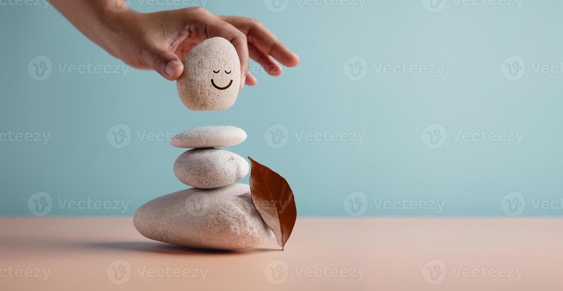 Enjoying Life Concept. Harmony and Positive Mind. Hand Setting Natural Pebble Stone with Smiling Face Cartoon to Balance on Beach Sand. Balancing Body, Mind, Soul and Spirit. Mental Health Practice photo