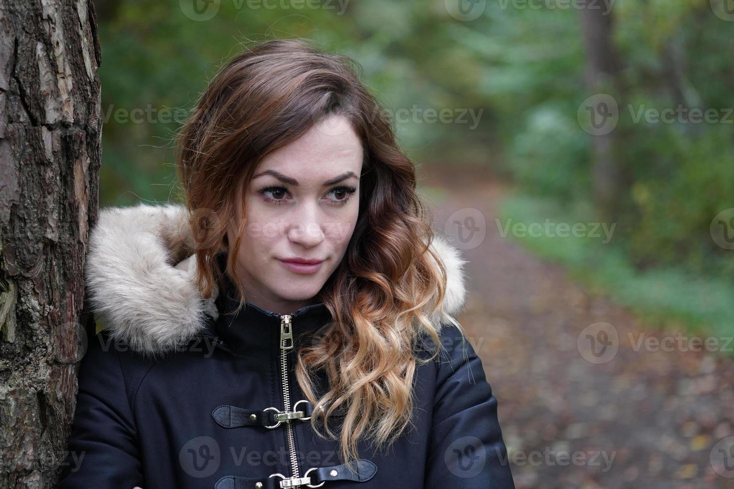 pensive young woman leaning against tree in forest photo