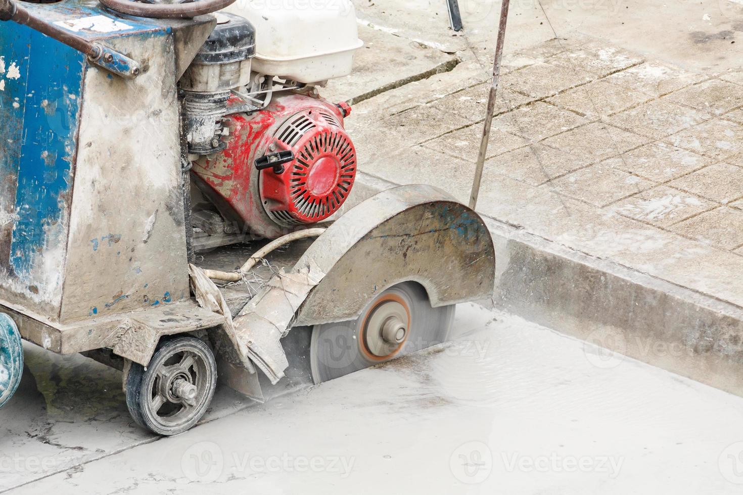 Worker using diamond saw blade machine cutting concrete road at construction site photo