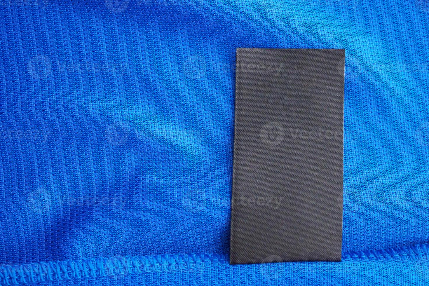 Black blank laundry care clothes label on blue jersey polyester sport shirt background photo