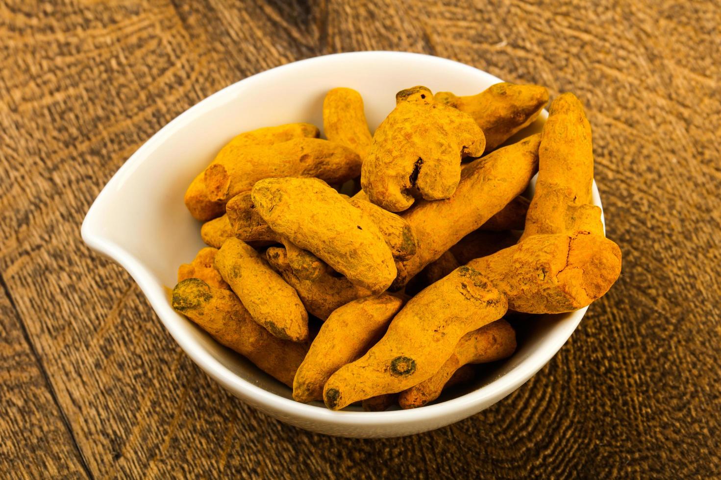 Tumeric roots in a bowl on wooden background photo