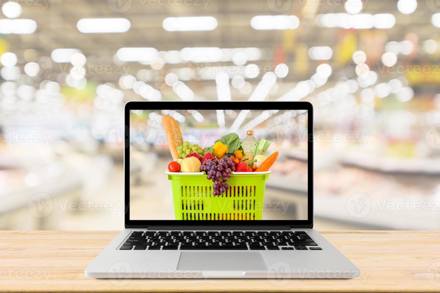 supermarket aisle blurred background with laptop computer and shopping basket on wood table grocery online concept photo