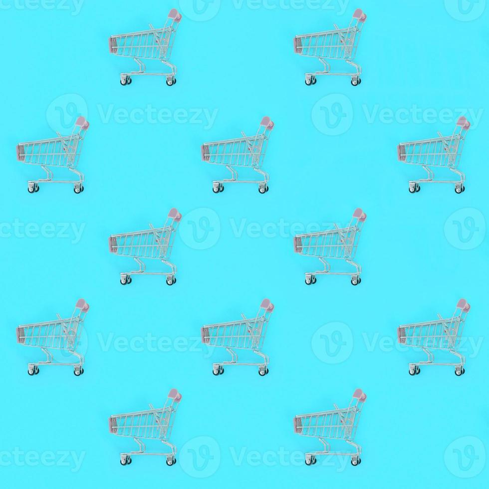 Shopping addiction, shopping lover or shopaholic concept. Many small empty shopping carts perform a pattern on a pastel colored paper background. Flat lay composition, top view photo