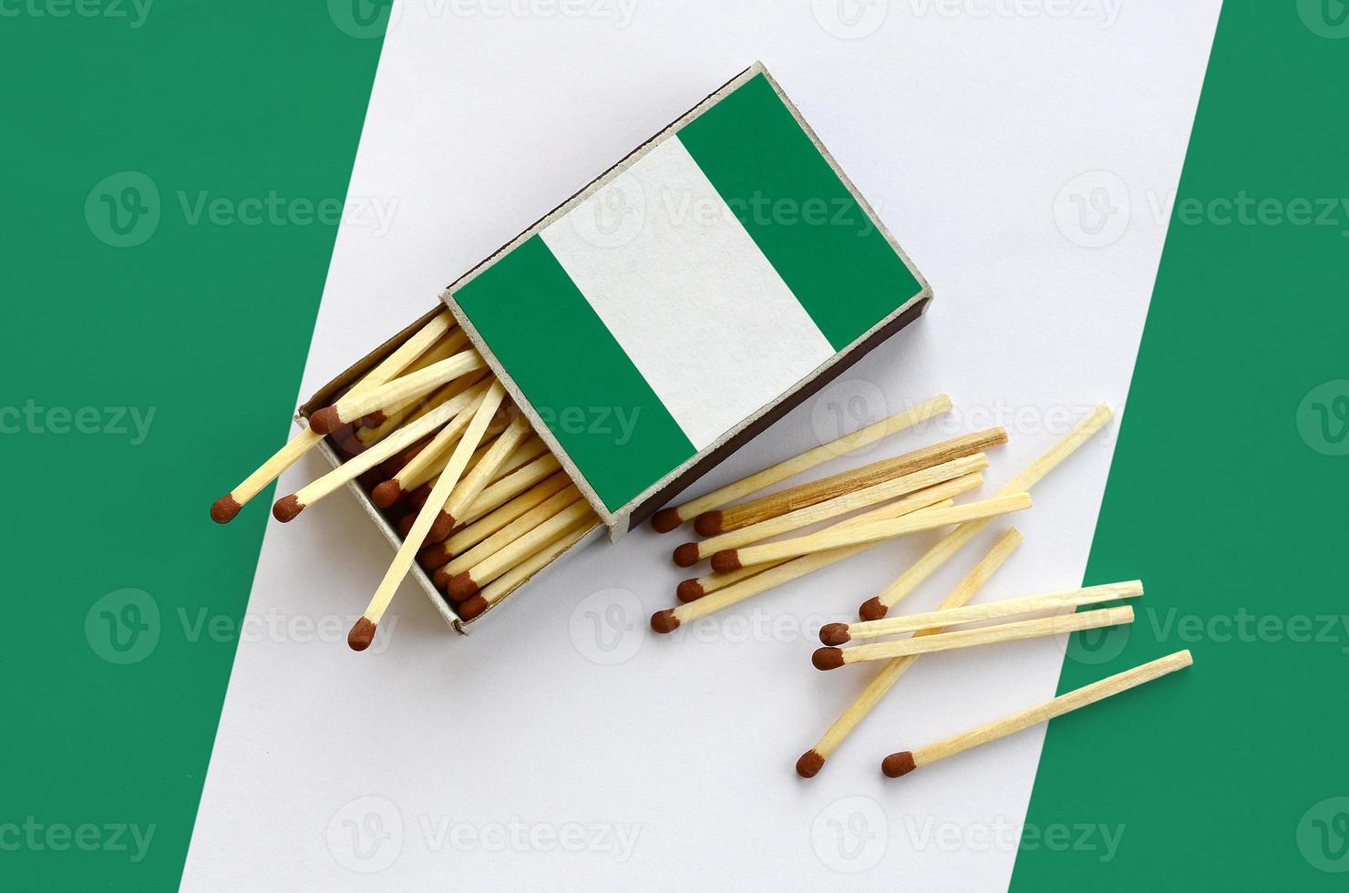 Nigeria flag  is shown on an open matchbox, from which several matches fall and lies on a large flag photo