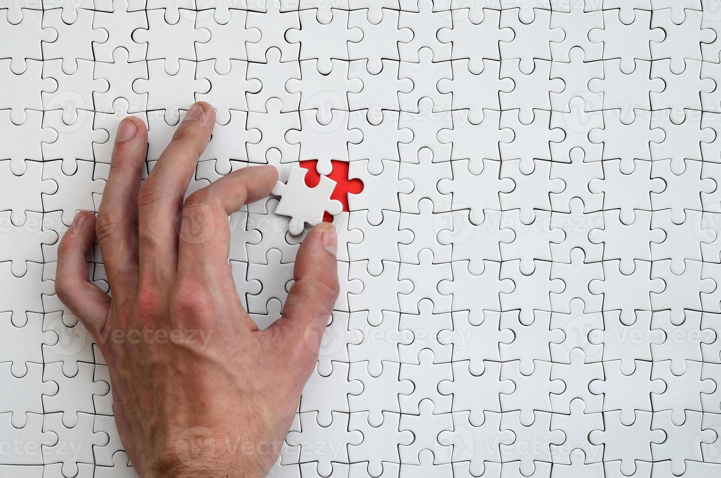 The texture of a white puzzle puzzle in the assembled state with one missing element that the male hand puts in photo