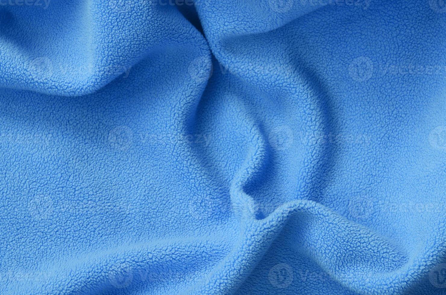 The blanket of furry blue fleece fabric. A background of light blue soft plush fleece material with a lot of relief folds photo