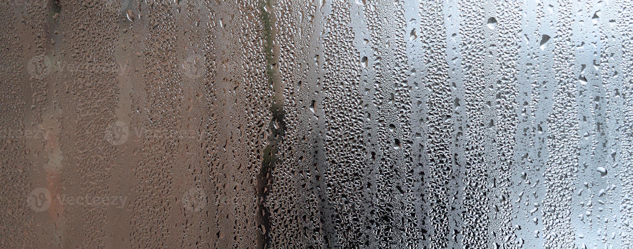 textura de una gota de lluvia sobre un fondo transparente húmedo de vidrio. tonificado en color gris foto